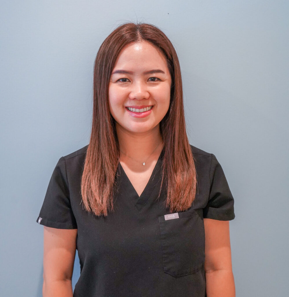 Professional headshot of female dentist Dr. Peggy Chuang smiling warmly in black scrubs against a soft blue background.
